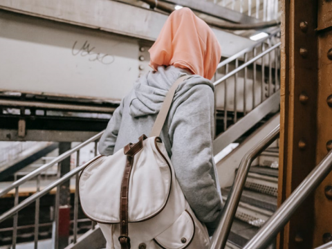 Woman wearing a hijab, hoodie and carrying a backpack ascending stairs in a station