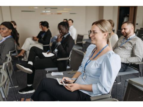 A selection of employees in a large meeting, all facing forwards towards a presenter