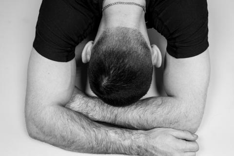 a black and white photo of a white man in a black t-shirt with his head in his arms