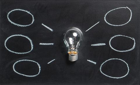 a light bulb on a chalk board with small circles in chalk written around it