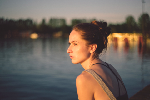 a woman in profile sits next to a river and looks towards the distance