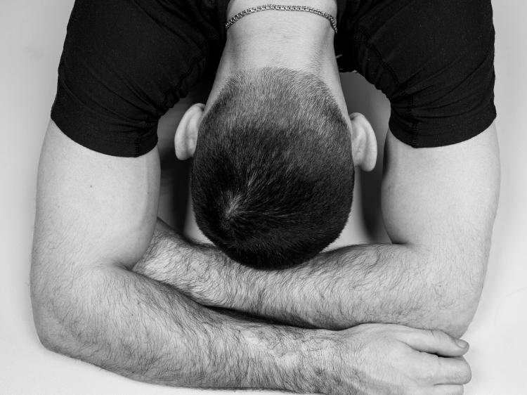 a black and white photo of a white man in a black t-shirt with his head in his arms