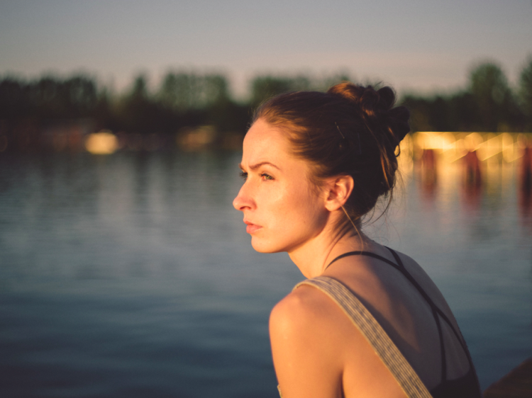 a woman in profile sits next to a river and looks towards the distance